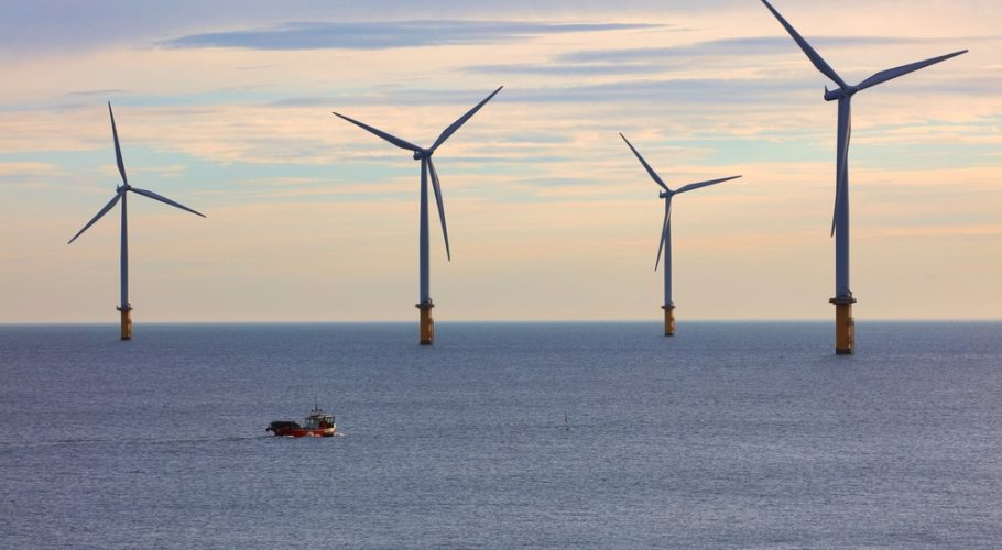 Small,Fishing,Boat,Dwarfed,By,Huge,Wind,Turbines,Off,The